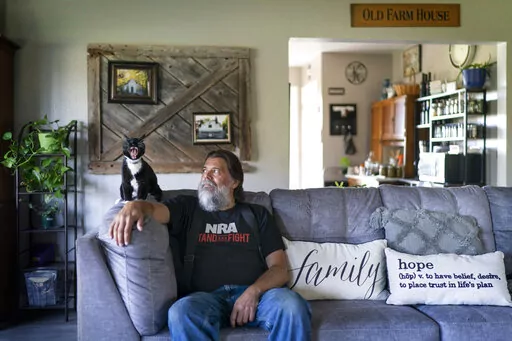 John Kraft sits next to his yawning cat, Tux, at his hilltop farmhouse in Clear Lake, Wis., Wednesday, Sept. 28, 2022. Kraft loves this place. He loves the quiet and the space but looks beyond his rural community and sees a country that many Americans wouldn't recognize. It's a dark place, dangerous, where democracy is under attack by a tyrannical government, few officials can be trusted and clans of neighbors might someday have to band together to protect one another. (AP Photo/David Goldman)