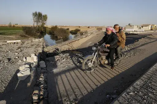 Syrian citizens ride a motorcycle as they cross a bridge that links to Lebanon which was destroyed on Oct. 24 by an Israeli airstrike, in Qusair, Syria, Sunday, Oct. 27, 2024. (AP Photo/Omar Sanadiki)