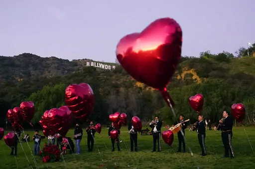 A Mexican Mariachi band surrounded by heart-shaped balloons awaits the arrival of a couple's wedding proposal ceremony at the Lake Hollywood Park in Los Angeles, on Valentine's Day, Monday, Feb. 14, 2022. Attending weddings can be expensive, between travel and lodging, gifts and extra events like bachelor and bachelorette parties. So plan ahead for these expenses, particularly as wedding season approaches and celebrations that were postponed or rescheduled reappear on your calendar.   (AP Photo/