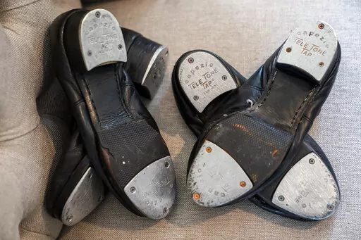 Old tap shoes rest on a chair as Gary Schaufeld describes his time as a young performer in dance competitions, Thursday, Feb. 10, 2022, at his home in Port Jefferson, N.Y. He was a teen in 2004, assisting a successful tap dancer named Danny Wallace. Schaufeld had fallen in love with tap at 7 years old, and assisting Wallace offered a chance to raise his profile and learn from one of the best. (AP Photo/John Minchillo)