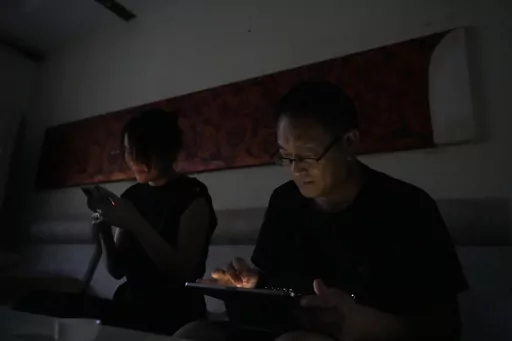 Wang Quanzhang and his wife Li Wenzu look at their phone and laptop in the dark after power was cut off for their apartment in Beijing's Changping district, Tuesday, June 20, 2023. Disbarred human rights lawyer Wang Quanzhang has been forced to move 13 times in two months as part of a pattern of harassment against him and three other prominent rights advocates in Beijing that is further squeezing the country's battered civil rights community. (AP Photo/Ng Han Guan)