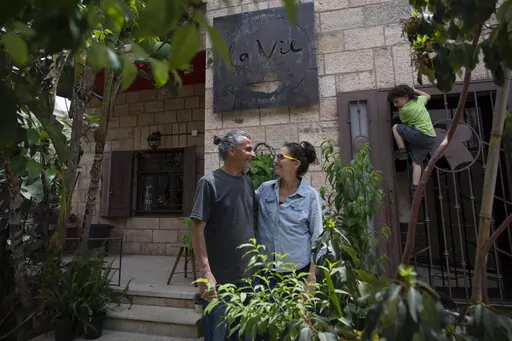 Kenae Totah, 5, right, plays while his parents Morgan Cooper, 41, center and foreign spouse Saleh Totah, right, pose for a photo in front of their restaurant, at the West Bank city of Ramallah, Monday, May 2, 2022. Israel published a new set of rules and restrictions Sunday, Sept. 4, 2022, for foreigners who want to enter or live in Palestinian areas of the West Bank, including a requirement that people who form romantic relationships with local Palestinians register with Israeli authorities. (A