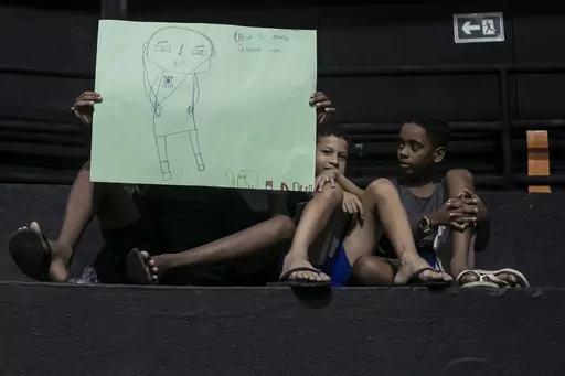 Children hold drawings that represent their experiences of living in the Mare favela at an event to launch the book titled “I was supposed to be at school” in the Mare favela of Rio de Janeiro, Brazil, Monday, March 25, 2024. Dozens of kids and teenagers from one of Rio de Janeiro's most violent favelas gathered on Monday to celebrate their most important piece of work yet: a book that aims to show authorities how they see police violence in their Maré community from a young age. (AP Photo/