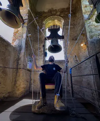 +++ON HOLD++++ Sitting in a chair with ropes looped around both feet and hands, Joan Carles Osuna, a student of the Vall d'en Bas School of Bell Ringers, performs playing all four bronze bells at the church bell tower of the12th-century Sant Romà church, at the village of Joanetes, about two hours north of Barcelona, Spain, Saturday, July 29, 2024. A school set up to revive the manual ringing of church bells has graduated its first class of 18 students after learning their ringing skills. (AP P