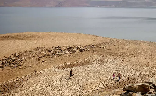 FILE — In this Aug. 22, 2021, file photo, a family walks over cracked mud near Lake Oroville's shore as water levels remain low due to continuing drought conditions in Oroville, Calif. State water officials are preparing to tell major urban and agricultural water agencies on Friday, March 18, 2022, that they'll get even less water from state supplies than the small amount they were promised at the start of the year. Lake Oroville is currently 68% of its historical average supply.(AP Photo/Etha