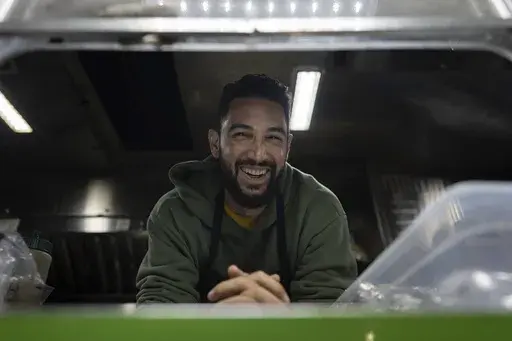 World Central Kitchen Chef Corp member Daniel Shemtob smiles as he looks out from the service window of his food truck, The Lime Truck, as he serves burritos to Eaton Fire first responders at the Rose Bowl Stadium, Wednesday, Jan. 15, 2025, in Pasadena, Calif. (AP Photo/Carolyn Kaster)