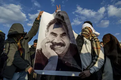Youngsters hold a photograph of the jailed leader of the rebel Kurdistan Workers' Party, or PKK, Abdullah Ocalan as they gather to watch live on a tv screen a Pro-Kurdish Peoples' Equality and Democracy Party, or DEM, delegation members releasing an statement from Ocalan, in Diyarbakir, Turkey, Thursday, Feb. 27, 2025. (AP Photo/Metin Yoksu)
