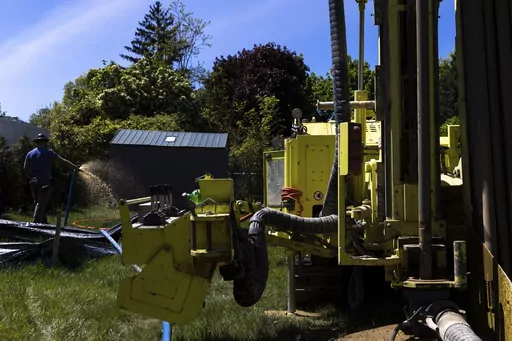 A Dandelion Energy employee sprays excess groundwater back on the lawn during installation of a geothermal heat pump system at a home in White Plains, N.Y., Monday, May 8, 2023. A water-filled loop is installed several hundred feet deep in the yard to either carry heat away from or into the house depending on season. Industry experts see the technology becoming increasingly popular in the coming years. (AP Photo/Julia Nikhinson)