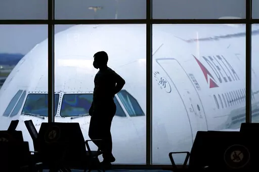 A passenger wears a face mask to help prevent the spread of the new coronavirus as he waits for a Delta Airlines flight at Hartsfield-Jackson International Airport in Atlanta on Feb. 18, 2021.  Flight attendants are about to get an extra hour of required rest between shifts. The Federal Aviation Administration said Tuesday, Oct. 4, 2022, that it will require the workers get at least 10 hours off between shifts, fulfilling a requirement that Congress approved in 2018.   (AP Photo/Charlie Riedel, 