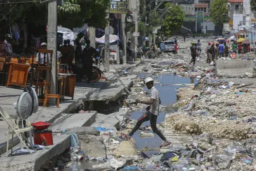A man crosses a storm drain filled with trash in Port-au-Prince, Haiti, Friday, Sept. 13, 2024. (AP Photo/Odelyn Joseph)