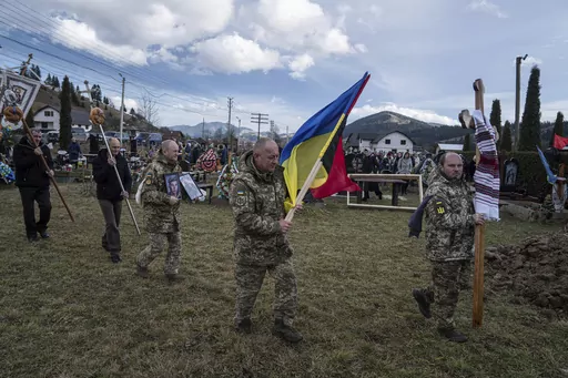 Ukrainian servicemen carry national flags and photos of their comrade Vasyl Boichuk who was killed in Mykolayiv in March 2022, during his funeral ceremony at the cemetery in Iltsi village, Ukraine, Tuesday, Dec. 26, 2023. (AP Photo/Evgeniy Maloletka)