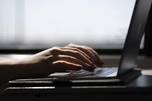 This May 18, 2021, photo shows a person typing on a laptop on a train in New Jersey. (AP Photo/Jenny Kane, File)