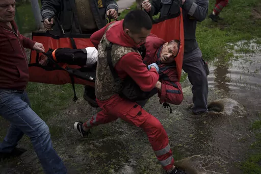 An emergency worker is helped by locals to carry an injured man who missing a part of his leg to an ambulance following a Russian bombardment in Kharkiv, Ukraine, Wednesday, April 27, 2022. (AP Photo/Felipe Dana)