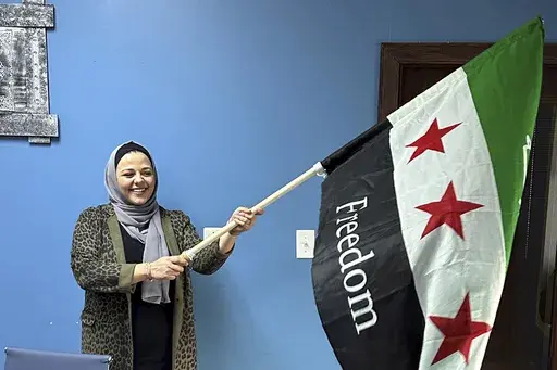 Rama Alhoussaini holds a Syrian flag in her Dearborn Heights, Mich., office, Tuesday, Dec. 10, 2024. (AP Photo/Corey Williams)