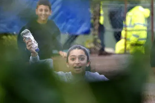 A young girl runs towards the fence carrying a message in a bottle inside the Manston immigration short-term holding facility located at the former Defence Fire Training and Development Centre in Thanet, England, Wednesday, Nov. 2, 2022. Details about overcrowding and inhumane conditions at a migrant processing center in southeast England have shocked Britain and reignited a heated debate about how the Conservative government is handling a sharp increase in the number of asylum-seekers arriving 