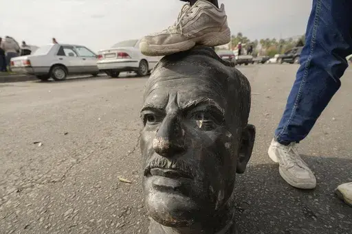 An opposition fighter steps on a broken bust of the late Syrian President Hafez Assad in Damascus, Syria, on Sunday Dec. 8, 2024. (AP Photo/Hussein Malla)
