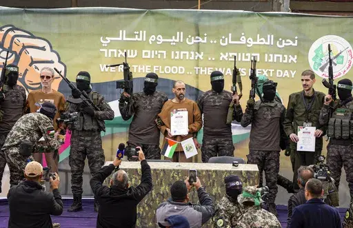 Israeli captives, from left to the right, Ohad Ben Ami, Eli Sharabi and Or Levy, who have been held hostage by Hamas in Gaza since Oct. 7, 2023, are escorted by Hamas fighters on a stage before being handed over to the Red Cross in Deir al-Balah, central Gaza Strip, Saturday, Feb. 8, 2025. (AP Photo/Abdel Kareem Hana)