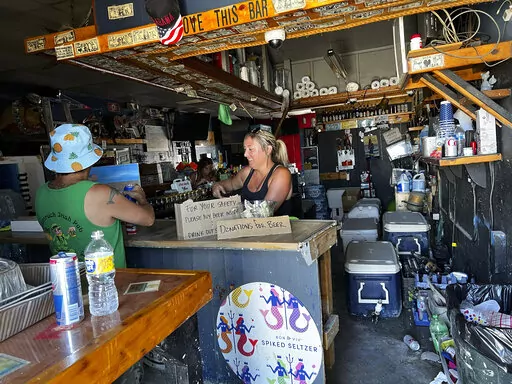 Ashley Galassi, a bartender at Tina’s, a watering hole at Fisherman’s Wharf in Fort Myers, Florida, attends to a patron on Friday, Oct. 7, 2022. She says the bar will likely be demolished and reopen elsewhere. Hurricane Ian might have come and gone, but it has done long-term damage to the small businesses of a region heavily dependent on tourists and seasonal residents.  (AP Photo/Bobby Caina Calvan)