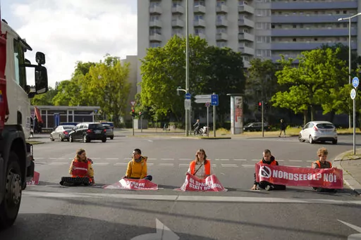 Climate activist Lina Schinkoethe, left, and her mother Solvig Schinkoethe, second from left, sit with their hands glued to the ground during a protest with the group Uprising of the Last Generation in Berlin, Germany, Tuesday, June 21, 2022. The group claims the world has only a few years left to turn the wheel around and avoid catastrophic levels of global warming.  (AP Photo/Markus Schreiber)