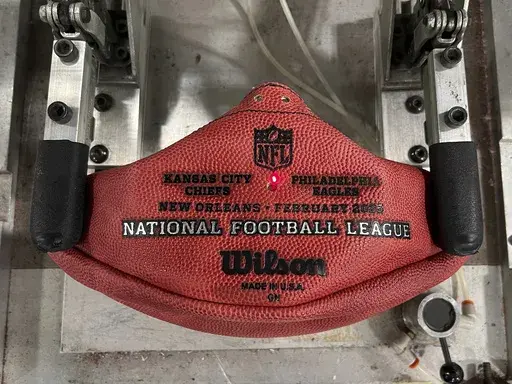 A machine imprints the names of the Philadelphia Eagles and the Kansas City Chiefs onto a football for the upcoming Super Bowl matchup at the Wilson Sporting Goods football factory, Monday, January 27, 2025, in Ada, Ohio. (AP Photo/Patrick Aftoora-Orsagos)