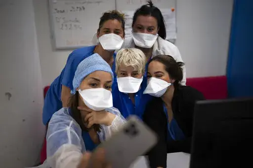 Hospital workers pose for a selfie together in the COVID-19 intensive care unit of the la Timone hospital in Marseille, southern France, Saturday, Dec. 25, 2021. Marseille’s La Timone Hospital, one of France’s biggest hospitals, has weathered wave after wave of COVID-19. (AP Photo/Daniel Cole)