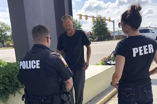 Chesterfield Patrol Officer Travis Adams, left, and peer recovery specialist Joy Bogese, right, talk with Adam Hall as part of Project Recover, in Chesterfield County, Va., Monday, Aug., 29, 2022. Project Recover is a program that embeds recovering addicts with police and ambulance crews in central Virginia to respond to overdose calls and to go on patrol to reach out to people struggling with drug addiction to try to get them into treatment programs. (AP Photo/Denise Lavoie)