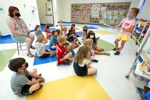FILE — Kelly Sheridan, left, and her first grade students wear face masks as one of the students makes a presentation during class in a hallway at the Milton Elementary School, May 18, 2021, in Rye, N.Y. The New York State Education Department is telling schools to continue to require masks despite a judge’s ruling overturning the state's mask mandate.  But some school districts already are rushing to drop the requirement.  The Education Department said in a statement Tuesday, Jan. 25, 202