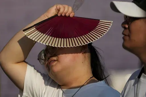 A woman uses a fan as she walks with her companion on a hot day in Beijing, June 16, 2024. June 2024 was the hottest June on record, according to Europe's Copernicus climate service on Monday, July 8. (AP Photo/Andy Wong, File)