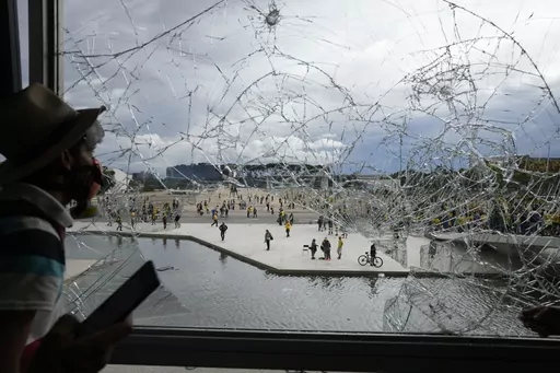 A protester, supporter of Brazil's former President Jair Bolsonaro, looks out from a shattered window of the Planalto Palace after he and many others stormed it, in Brasilia, Brazil, Jan. 8, 2023. Members of the three branches of power in Brazil say the country’s democracy and its guardrails have been restored after the trashing of the government buildings a year ago. But arrests have led supporters of the former president to say their freedom of speech is being violated and claim they are pol