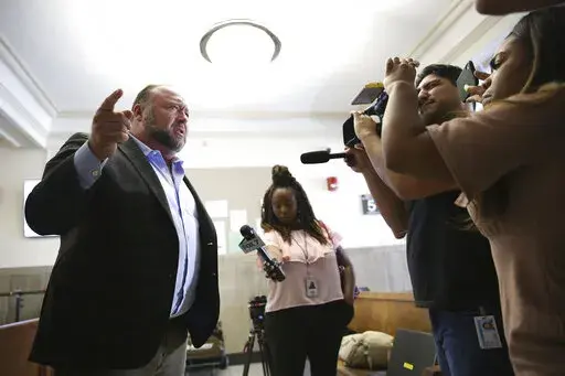 Alex Jones talks to media during a midday break during the trial at the Travis County Courthouse in Austin, Texas, Tuesday, July 26, 2022. An attorney for the parents of one of the children who were killed in the Sandy Hook Elementary School shooting told jurors that Jones repeatedly “lied and attacked the parents of murdered children” when he told his Infowars audience that the 2012 attack was a hoax. Attorney Mark Bankston said during his opening statement to determine damages against Jone