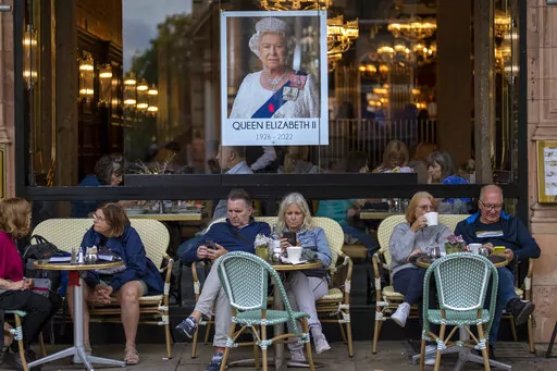 People sit at a terrace bar next to a portrait of Queen Elizabeth II in central London, Tuesday, Sept. 13, 2022. Hotels, restaurants and shops are packed as royal fans pour into the heart of London to experience the flag-lined roads, pomp-filled processions and brave a mileslong line for the once-in-a-lifetime chance to bid adieu to Queen Elizabeth II. (AP Photo/Emilio Morenatti, File)