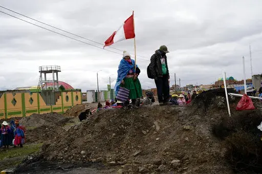An Aymara woman, holding a Peruvian national, stands on a pile of dirt serving as a roadblock set up by anti-government protesters, in Acora, southern Peru, Jan. 29, 2023. Peruvians have been protesting since early December, when former President Pedro Castillo was impeached after a failed attempt to dissolve Congress. His vice president, Boluarte, immediately took over — and has faced strong opposition ever since. (AP Photo/Rodrigo Abd, File)