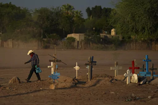 A Yaqui Indigenous wears a bandana over his mouth as he walks through dust past the cemetery where slain water-defense leader Tomás Rojo is buried in Potam, Mexico, Tuesday, Sept. 27, 2022. Rojo was a descendent of Tetabiate, a Yaqui leader killed in a 1901 battle with the government, which deported the surviving Yaquis to work in slave-like conditions on henequen plantations in far-away Yucatan. (AP Photo/Fernando Llano)