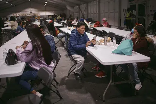 Migrant, Cesar Anibal Bonilla Estrada, 54, from Ecuador, center, checks his phone during dinner time at the migrant shelter on Randall's Island, on Tuesday, April 9, 2024, in New York. (AP Photo/Andres Kudacki, File)
