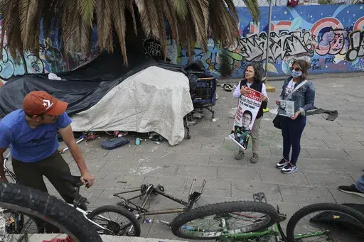 Catholic nun Paola Clericó, holding a poster of missing person Fernando Ivan Ornelas, and Veronica Rosas with a photo of her missing son Diego, ask a resident if he recognizes either man and invite him to join a Mass with members of their search collective "Uniendo Esperanzas" or Uniting Hope, in Mexico City, Sunday, July 21, 2024. The collective of people with missing family members held a Mass on the birthday of Ornelas who disappeared five years prior. (AP Photo/Ginnette Riquelme)