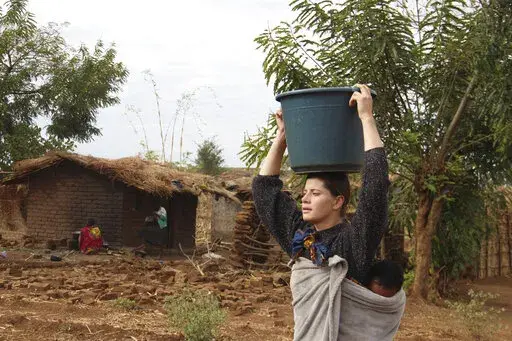 Cameron Beach, carries a carries a bucket of water on her head collected from a communal borehole in Dedza, near Lilongwe, Malawi, on July 23, 2021. Beach, a former Peace Corps volunteer, is living in rural Malawi teaching English at a rural high school where she had been sent by the United States government 18-months before COVID-19 began sweeping the world. The Peace Corps says it'll start sending volunteers overseas again in mid-March after it evacuated them from posts around the world two ye