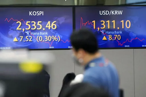A currency trader walks by screens showing the Korea Composite Stock Price Index (KOSPI), left, and the foreign exchange rate between U.S. dollar and South Korean won at a foreign exchange dealing room in Seoul, South Korea, Tuesday, Aug. 16, 2022. Asian shares mostly rose Tuesday after a rebound on Wall Street, despite regional investor risks reflected in negative economic data out of China. The benchmark in Tokyo was little changed, erasing earlier gains, but indexes in South Korea, Australia 