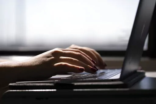 A woman types on a laptop while on a train in New Jersey, May 18, 2021. A trial of a four-day workweek in Britain, billed as the world's largest, has found that an overwhelming majority of the 61 companies that participated over six months last year will keep going with the shorter hours and that most employees were less stressed and burned out and had better work-life balance. (AP Photo/Jenny Kane, File)