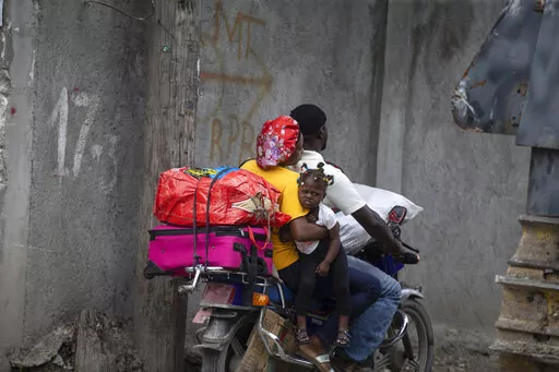Residents travel on a motorbike as they flee their home to avoid clashes between armed gangs, in the Croix-des-Mission neighborhood of Port-au-Prince, Haiti, Thursday, April 28, 2022. Experts say the scale and duration of gang clashes, the power they are wielding and the amount of territory they control has reached levels not seen before. (AP Photo/Odelyn Joseph)