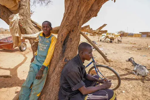 People lean on a tree in Djibo, Burkina Faso, Thursday May 26, 2022. African leaders have gathered for a summit in Malabo, Equatorial Guinea, to address growing humanitarian needs on the continent, which is also facing increased violent extremism, climate change challenges and a run of military coups. Leaders on Friday called for increased mobilization to resolve a humanitarian crisis that has left millions displaced and more than 280 million suffering from malnourishment. (AP Photo/Sam Mednick)
