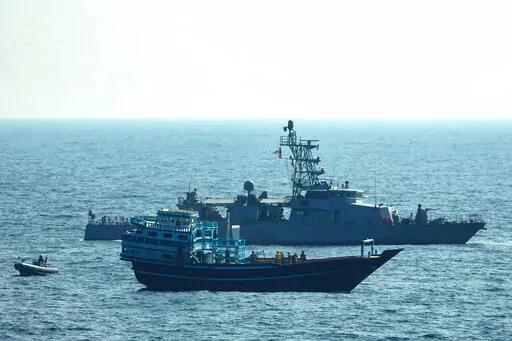 This photo released by the U.S. Navy, shows U.S. service members conduct a boarding on a stateless fishing vessel transiting international waters in the Gulf of Oman as a rigid-hull inflatable boat and patrol coastal ship USS Chinook (PC 9) sail nearby, Tuesday, Jan. 18, 2022. The U.S. Navy announced Sunday, Jan. 23 that it seized the boat in the Gulf of Oman carrying fertilizer used to make explosives that was caught last year smuggling weapons to Yemen. (U.S. Navy via AP)