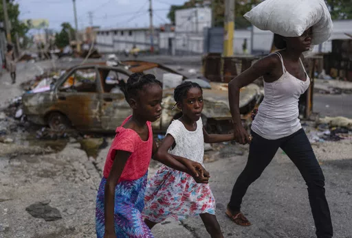 Girls holding hands are led past a burnt car blocking the street as they evacuate the Delmas 22 neighborhood to escape gang violence in Port-au-Prince, Haiti, May 2, 2024. As young Haitians are increasingly exposed to violence, the country is undergoing a wider push to dispel a long-standing taboo on seeking therapy and talking about mental health. (AP Photo/Ramon Espinosa, File)