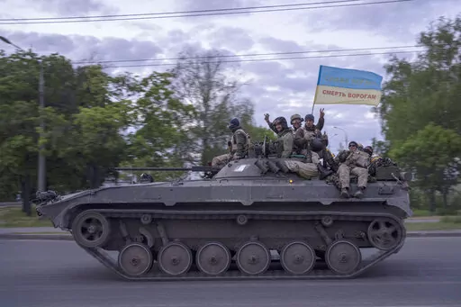 Ukrainian serviceman wave a flag with writing reading in Ukrainian "Glory to Ukraine", top, and "Death to the enemies"        as they ride atop of a tank in the Kharkiv region, eastern Ukraine, Monday, May 16, 2022. (AP Photo/Bernat Armangue)