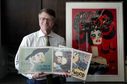 Dwight Cleveland, a major collector of movie posters and lobby cards, poses for a portrait with a three lobby card and movie poster Tuesday, Sept. 27, 2022, in Chicago. Many silent films from the early 1900s no longer exist. But they live on in movie theater lobby cards. More than 10,000 of the mostly 11-by-14-inch cards that promoted the cinematic romances, comedies and adventures of the era are being digitized for preservation and publication online, thanks to an agreement formed between a Chi