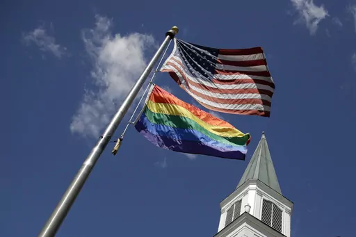 A gay Pride rainbow flag flies with the U.S. flag in front of the Asbury United Methodist Church in Prairie Village, Kan., on Friday, April 19, 2019. As of June 2023, more than 6,000 United Methodist congregations — a fifth of the U.S. total — have now received permission to leave the denomination amid a schism over theology and the role of LGBTQ people in the nation's second-largest Protestant denomination. (AP Photo/Charlie Riedel, File)