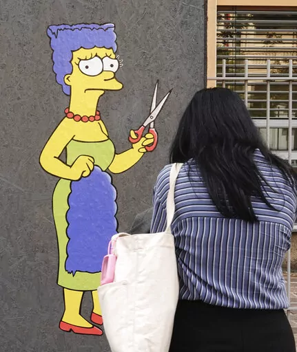 A woman takes pictures of a mural called "The Cut" by street artist aleXsandro Palombo depicting Marge Simpson, a character of the animated television series "The Simpsons" cutting her iconic hair, in front of the Consulate of Iran, in Milan, Italy, Wednesday, Oct. 5, 2022. Thousands of Iranians have taken to the streets over the last two weeks to protest the death of Mahsa Amini, a 22-year-old woman who had been detained by Iran's morality police in the capital of Tehran for allegedly not adher
